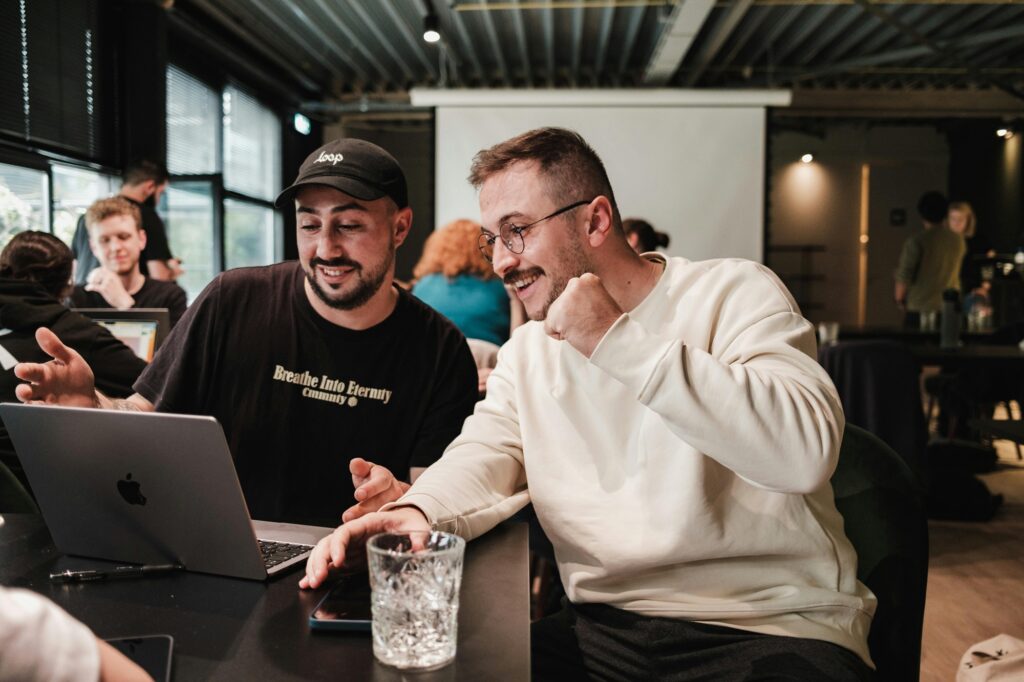 2 junge Männer unterhalten sich gut gelaunt, während sie auf einen Laptop schauen.